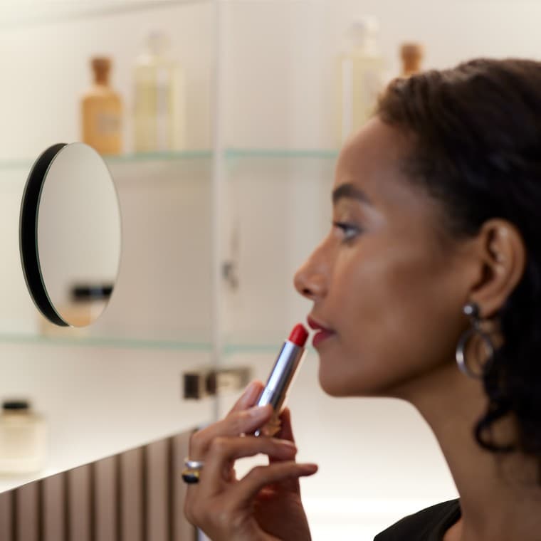 Sieviete uzklāj dekoratīvo kosmētiku, skatoties spogulī Sieviete uzklāj dekoratīvo kosmētiku, skatoties spogulī